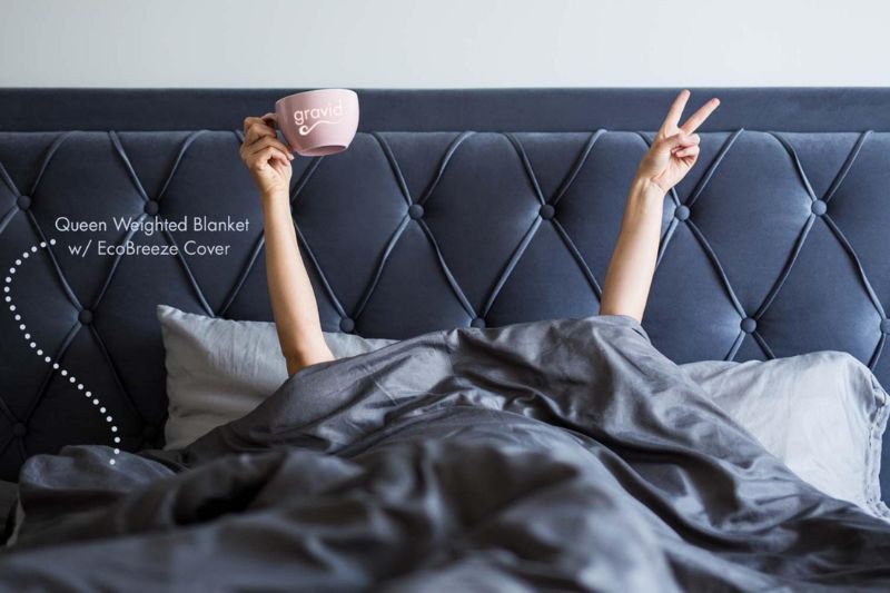 a lady lying under a weighted blanket with a cup of coffee