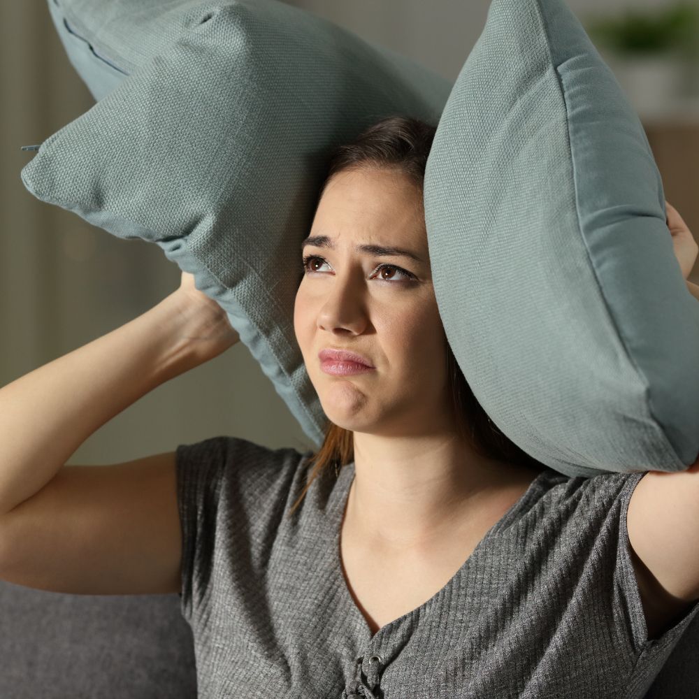 Woman trying to block out noise by holding pillows over her ears