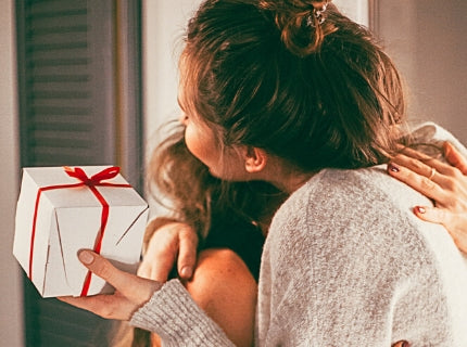 Woman receiving wrapped gift from another person and hugging