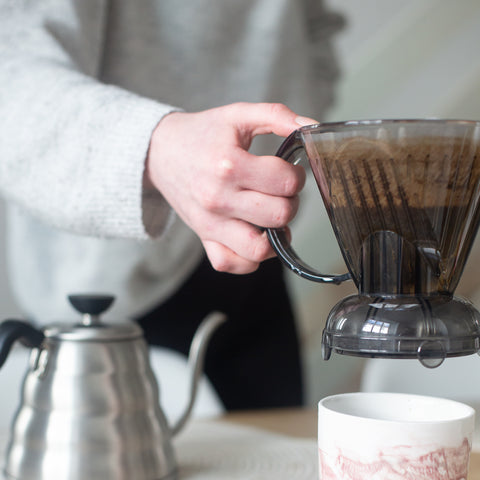 Person lifting a Clever Dripper coffee maker onto a cup 