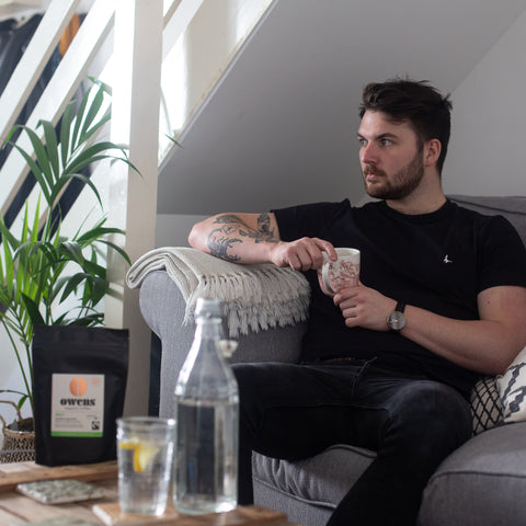 Man sat on couch in a lounge with cup of coffee