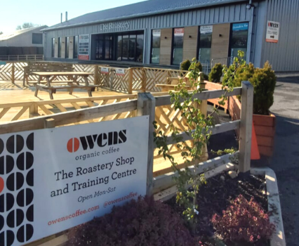 Owens Coffee sign in front of decking area with The Roastery building in background