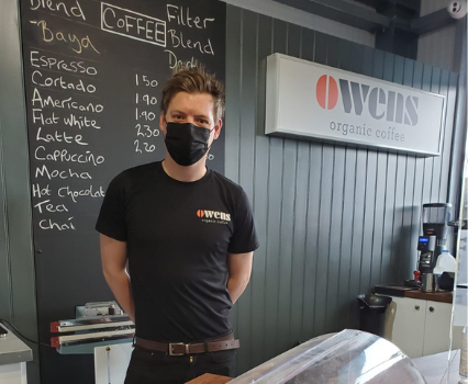 Team member of Owens Coffee stood in shop with sign in background