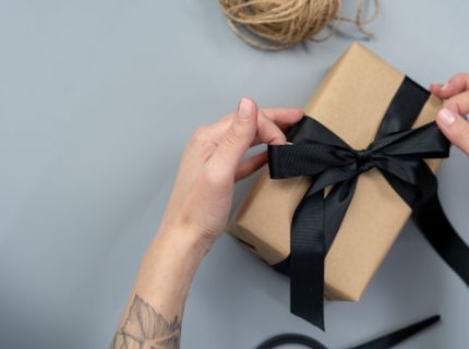Hands wrapping gift in brown paper and tying black ribbon