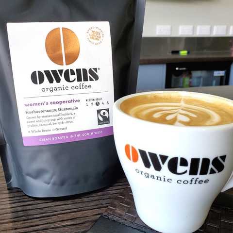 Bag of Owens Coffee Womens Cooperative Single Origin Coffee next to a mug with Owens Organic Coffee written on it and latte art in it