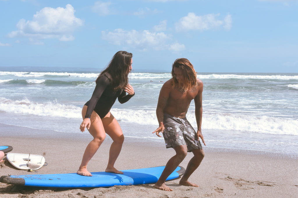 surf guide teaching a girl how to surf on the beach