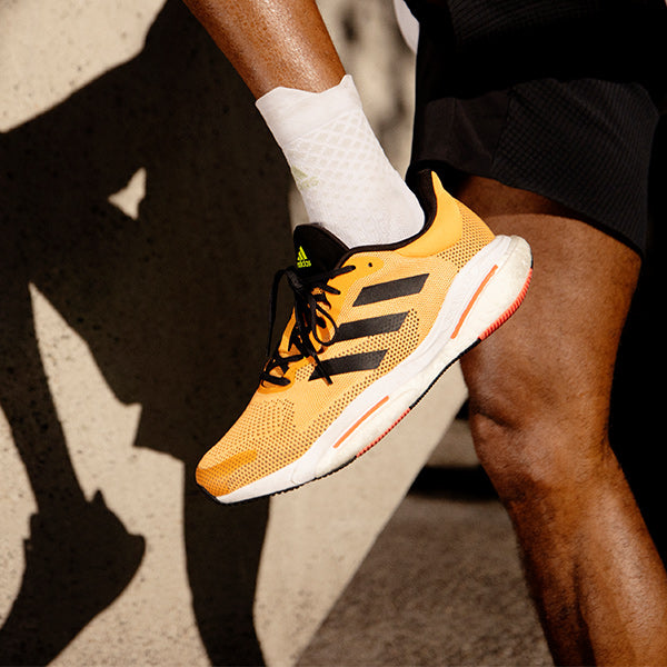 Close up of man stretching in orange, black and white adidas Solar Glide 5 running shoes