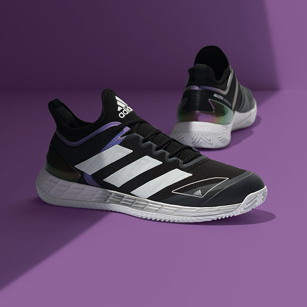 studio image of men's black and purple adidas tennis shoes on purple background