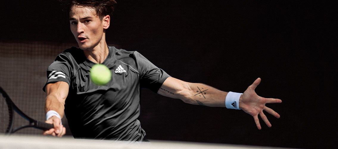 Action shot of man playing tennis in adidas tennis clothing and adidas tennis sweatband