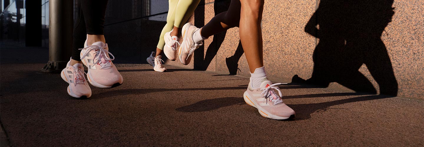 Three women running in white, silver and orange adidas Solar Glide 5 running shoes on a paved walkway