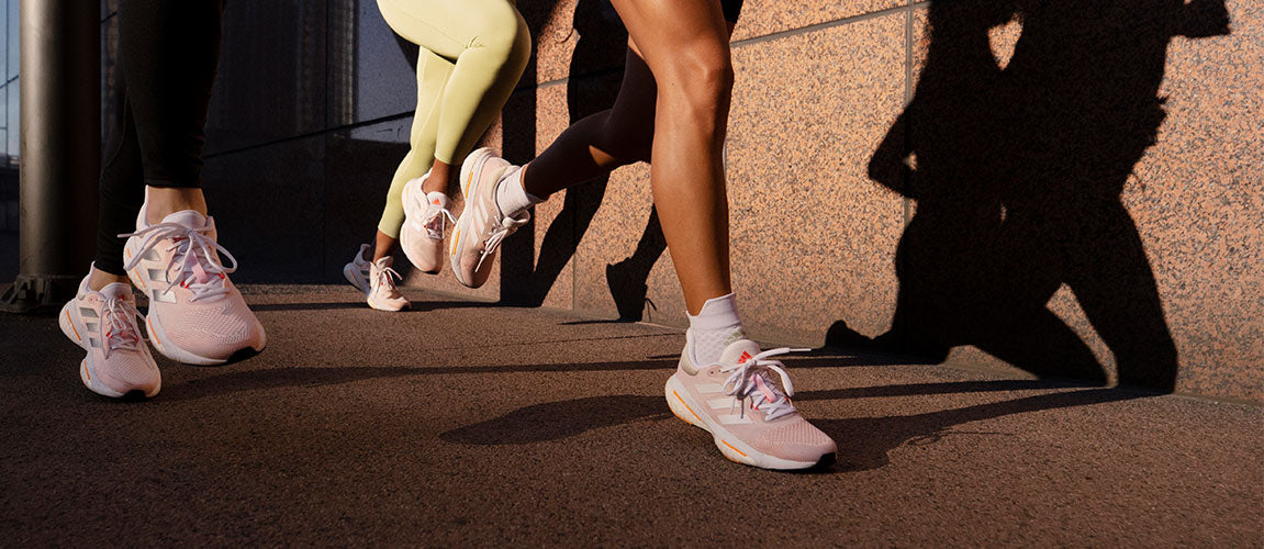 Three women running in white, silver and orange adidas Solar Glide 5 running shoes on a paved walkway