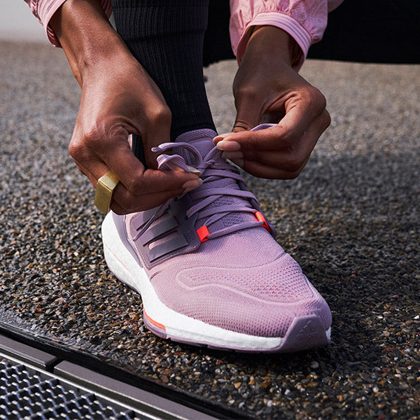 Close up of a woman tightening the laces of her purple and white adidas Ultraboost 22 running shoes