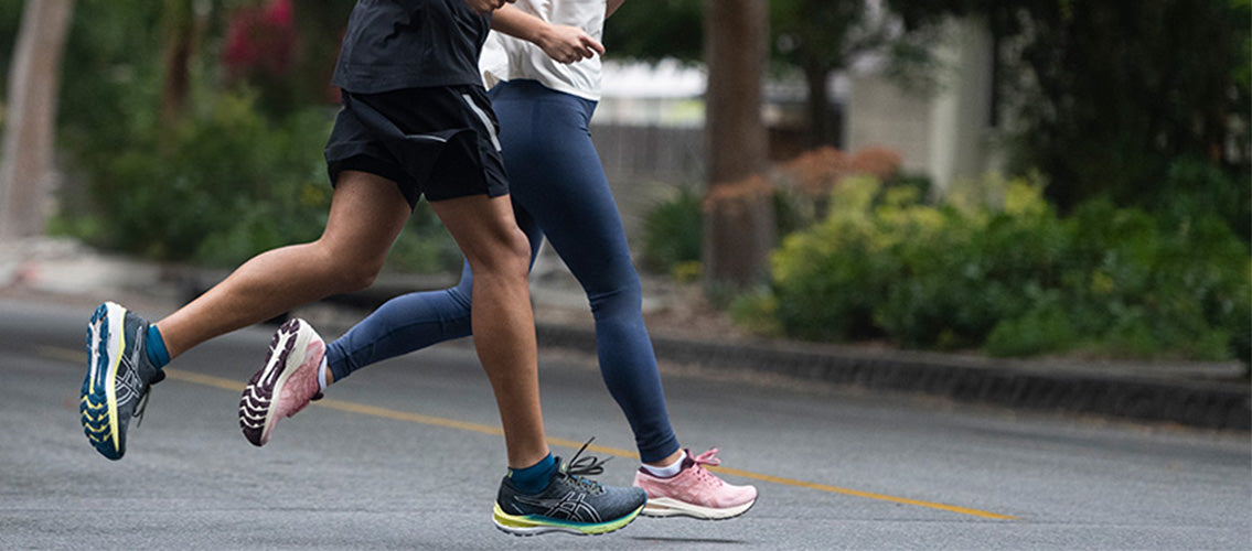 A man and a woman running across a residential street in ASICS running shoes and clothing