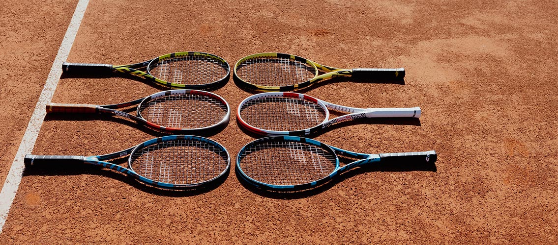 Babolat Pure Strike, Pure Aero and Pure Drive tennis racquets laying flat on a clay tennis court.
