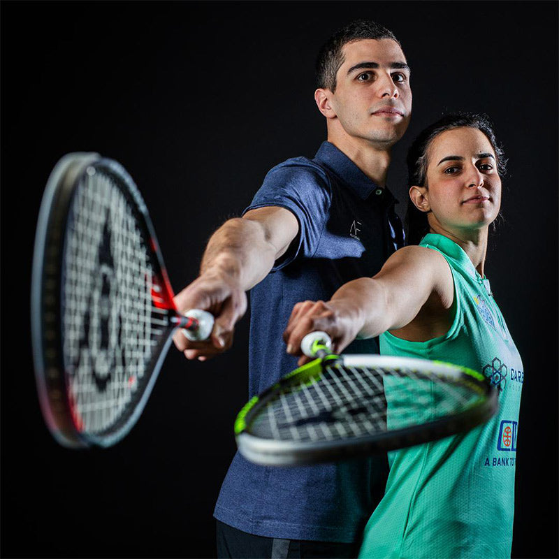 Man and woman standing together holding out squash racquets on black studio background