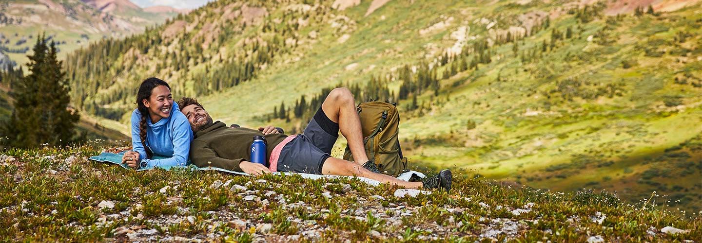 Man and woman happily lounging in scenic field while drinking from Hydro Flask bottles