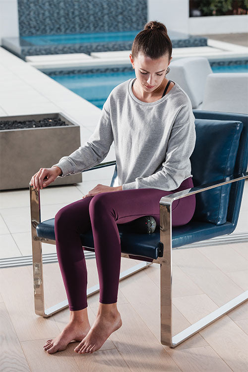 Woman sitting in chair using Hyperice Hypersphere mini for hamstring