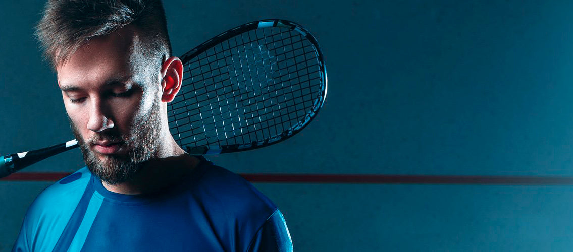 Man holding squash raquet behind blue studio background