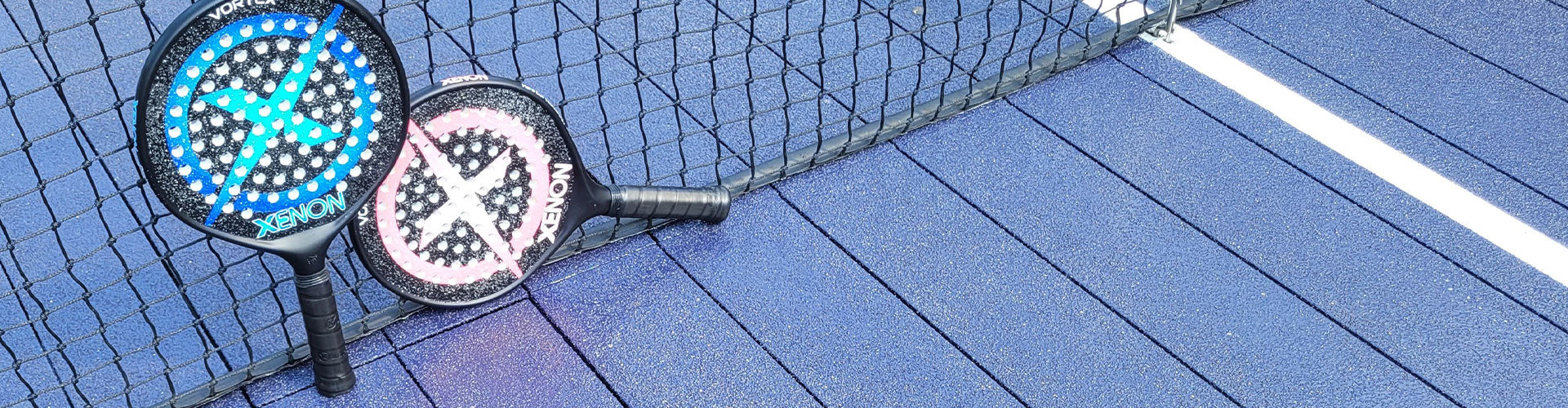 Blue and pink Xenon platform tennis paddles leaning on platform tennis net