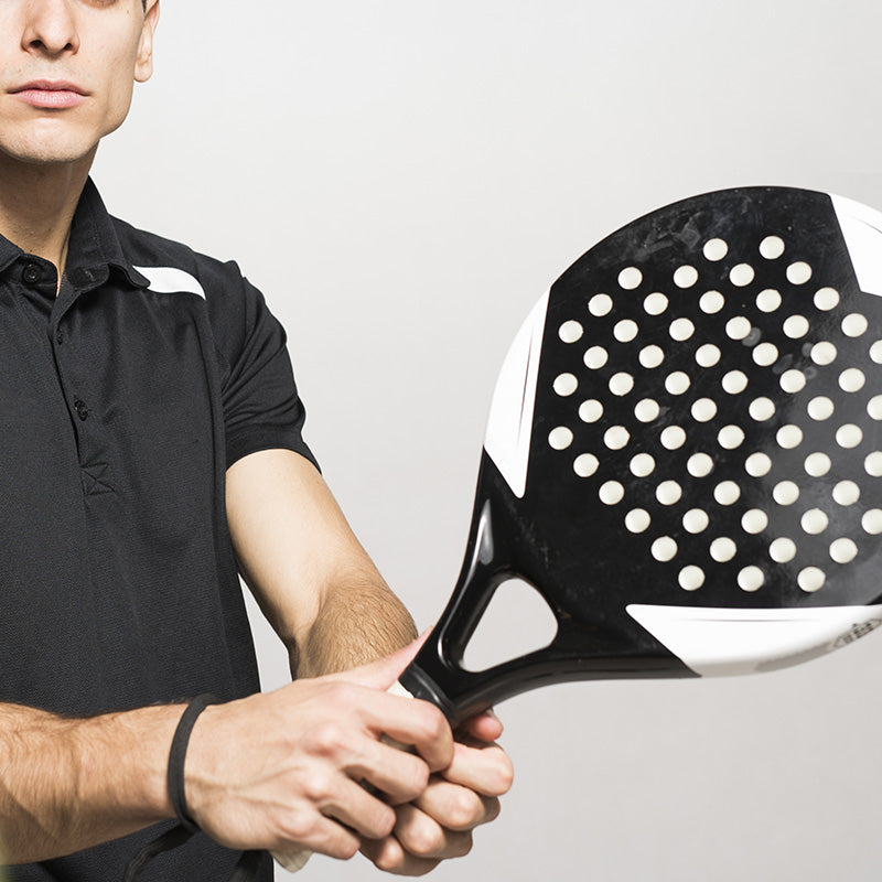 Man holding black and white platform tennis paddle in front of white studio background