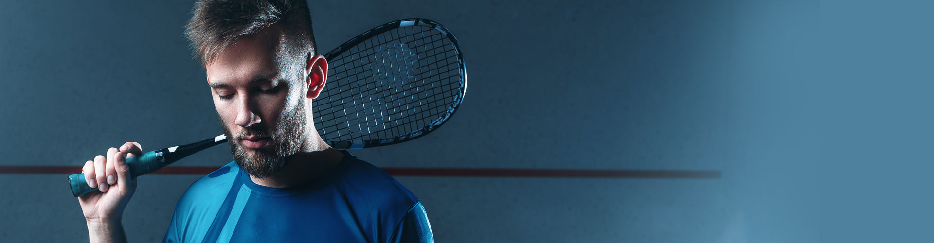 Man holding squash raquet behind blue studio background