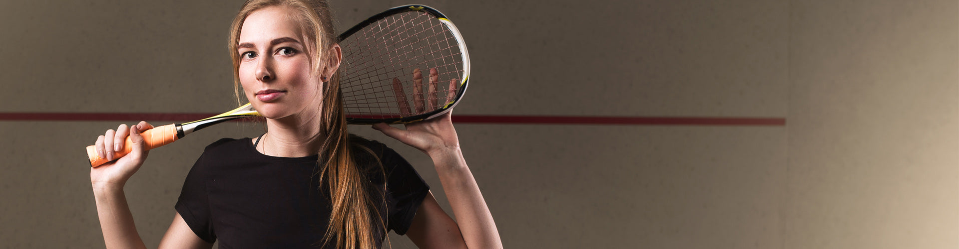 Woman smiling holding squash raquet behind black studio background