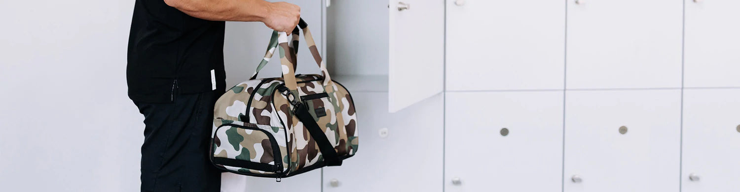 Man wearing all black outfit putting Vooray camo duffel in white gym locker