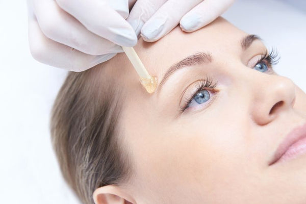 Woman getting eyebrows waxed with facial wax spatula