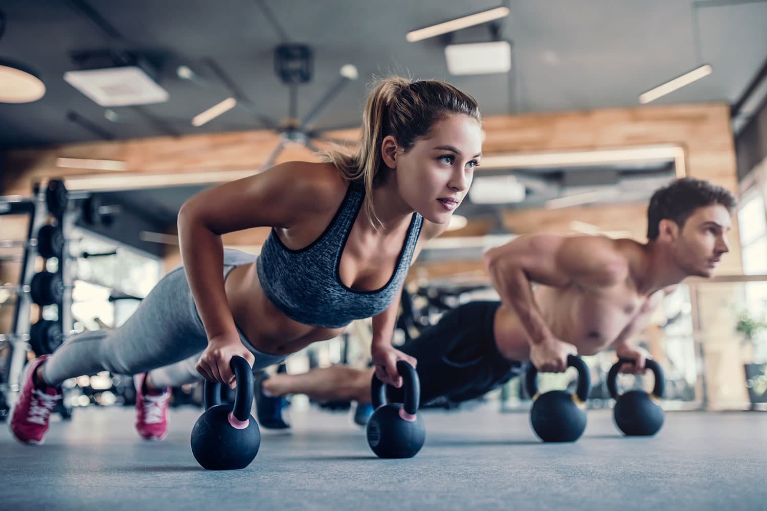 man and woman doing push ups on kettle bells at the gym