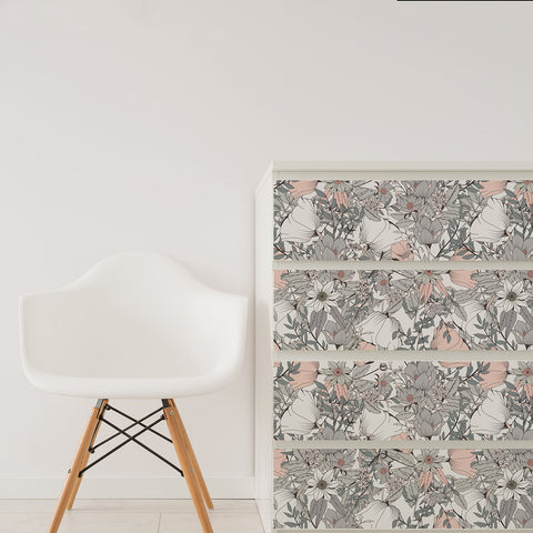 A white chair and IKEA Malm chest of drawers covered with custom grey and pink floral stickers