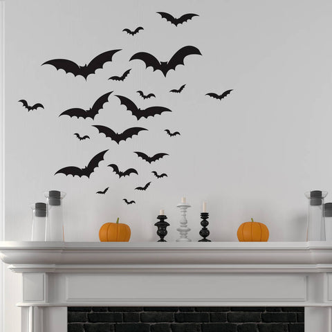 A white wall with a flock of black bat wall stickers over a white mantlepiece decorated for Halloween