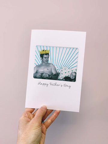 A picture of someone holding a card. The card has a photo on the front of a man and his baby. The card has embroidery on the front and the man is wearing a gold crown. It says Happy Father's Day underneath the photo