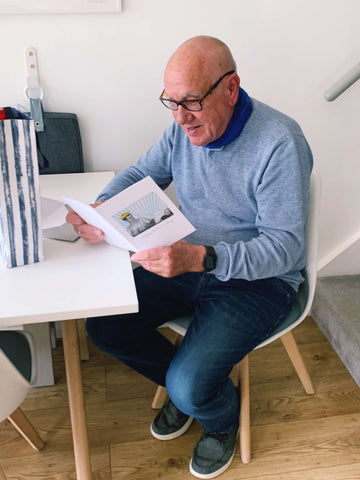 Picture of a man holding a father's day card and smiling. He is sat at a table and also have a gift bag next to him.