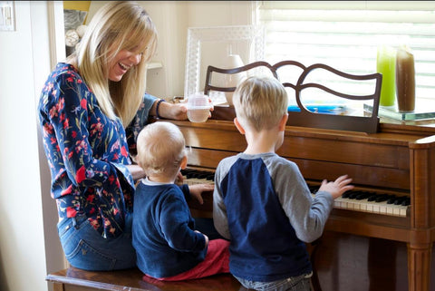 Jessica Bell sitting at a piano with her two children while holding a HaloVino wine tumbler.
