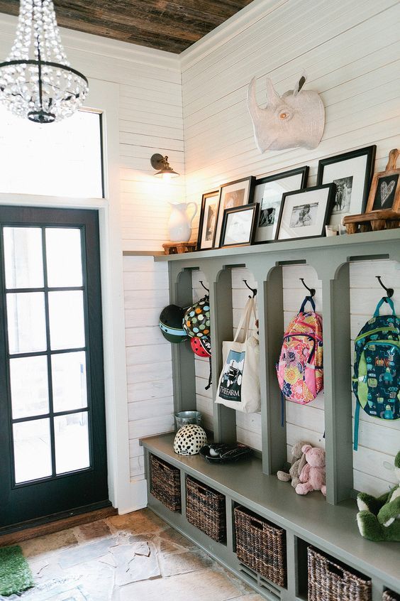Entryway with built-in wood bench with cubby holes and baskets, hooks with backpacks and a shelf with photographs