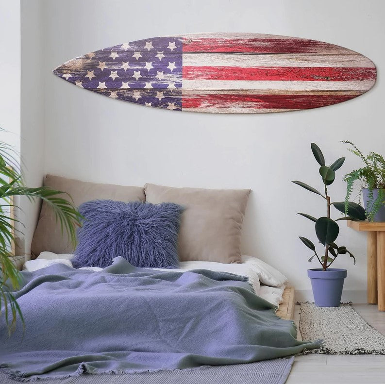 American Flag Wood Surfboard Plaque Wall Sign hanging on a wall in a bedroom above a bed with a blue pillow and blanket. 