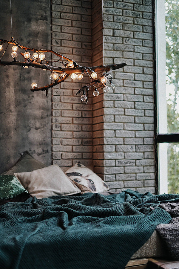 Bed with green cover next to a window and brick wall.