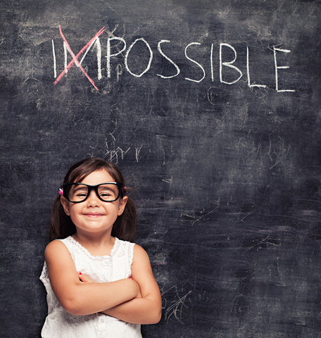 elementary age girl in front of a chalkboard with the word "impossible." The "Im" in "impossible" is crossed out.