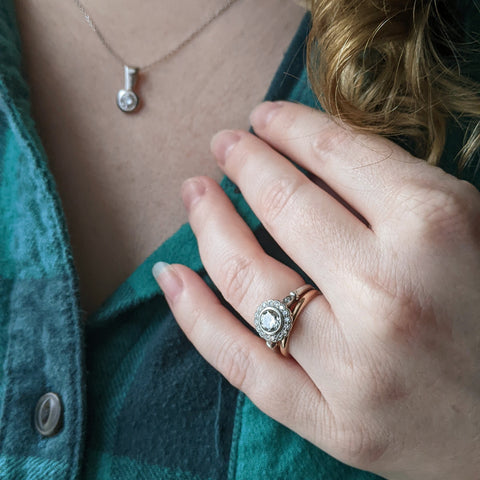 Antique-inspired halo engagement ring and wedding band in front of a green flannel shirt