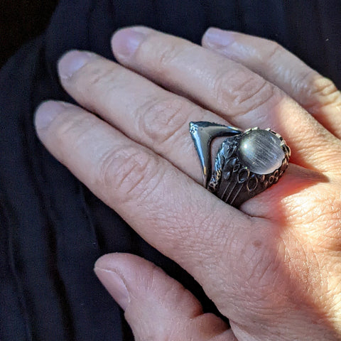 two blackened silver rings on a hand, atop a black pleated skirt