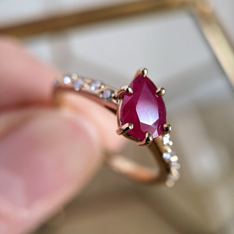 hand holding a yellow gold ring with an angled ruby pear center stone