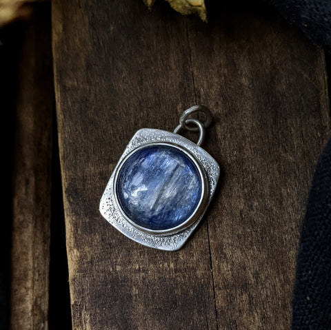 round blue gemstone pendant with a bezel setting and hammered silver background plate