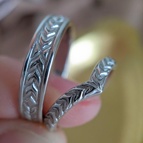 fingers holding two platinum wedding rings with a classic wheat engraving pattern