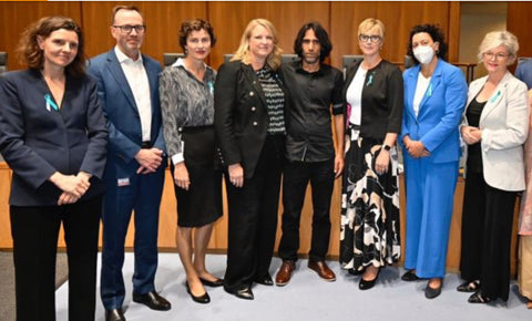 Seven parliamentarians stand in a line facing the camera with Behrouz Boochani in the centre