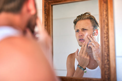 handsome young man looking closely at his skin in the mirror