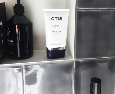 Otis Daily face Wash for Men pictured in a shower with shiny dark gray tiles