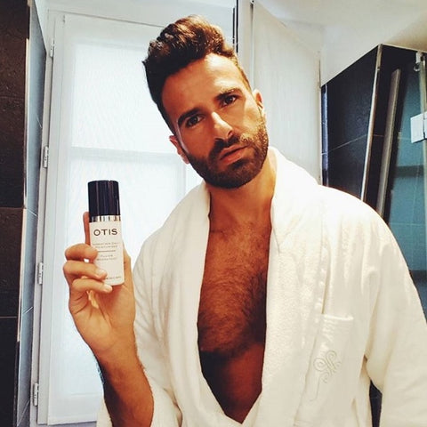 Handsome young bearded guy in white bathrobe holding moisturizer