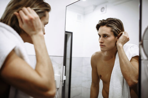 handsome young man looking in mirror at his smooth skin