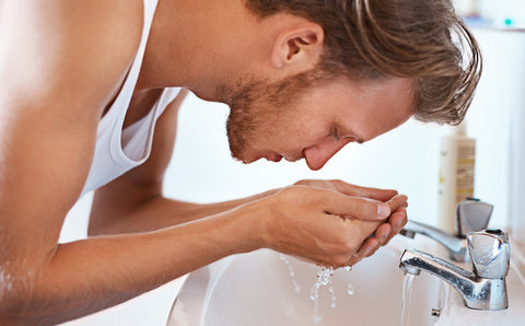 Handsome man washing his face, cupping his hands with water
