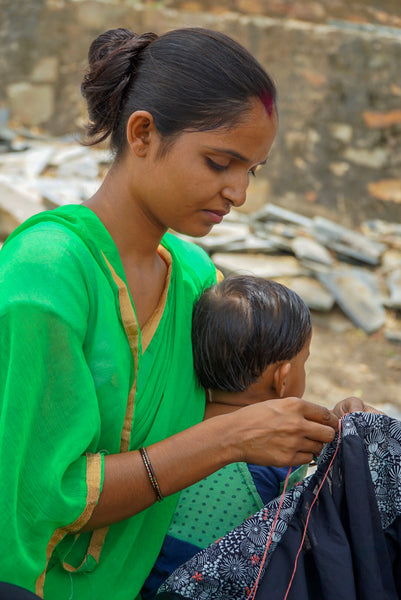 One of our artisans sitting with her son and hand stitching the Devi Embroidery Dress.